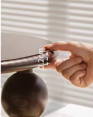 Hand meet de dikte van een ronde houten tafelblad – 2,2 cm dik massief hout, met zonlicht door jaloezieën op de achtergrond, ideaal voor productpresentatie of meubeldetails.