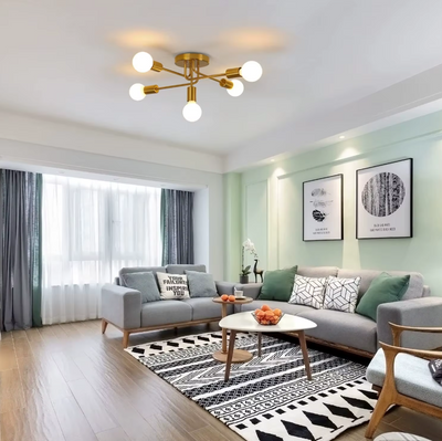 Industrieel-chique gouden plafondlamp met zes verstelbare armen en E27-LED-bollen, hangend boven ronde wit-houten salontafel met mandarijnen, grijze sofa’s met ‘FASHION HOME’-kussen op zwart-wit vloerkleed, in moderne woonkamer met lichtgroene muren, abstracte wanddecoratie en donkergroene gordijnen.