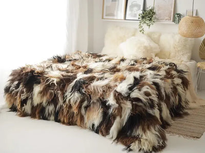 Dierenhuid in naturel kleuren met gevlekt patroon, gedrapeerd over een bed met witte kussens in een lichtrijke kamer met minimalistisch interieur
