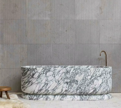 Vrijstaand bad van wit marmer met grijze aders, geplaatst tegen een moderne wand met verticale structuur – luxe badkamerdesign.