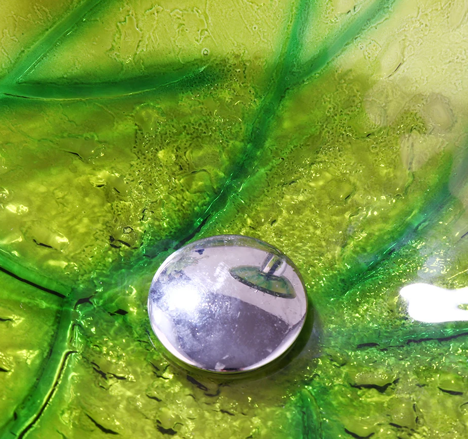 Close-up van groene glazen waskom met kraan en glinsterend oppervlak, detail van afvoer.