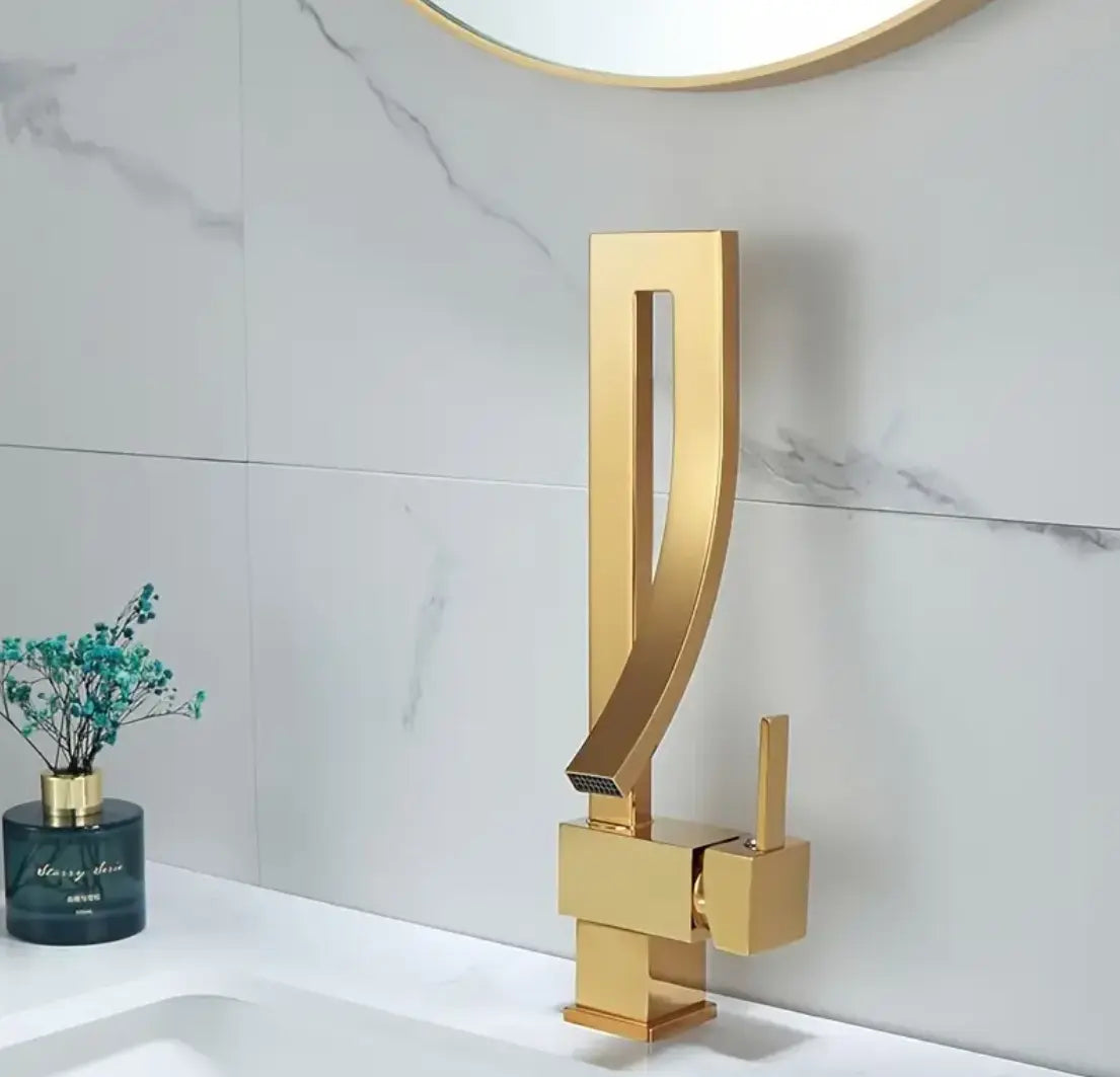 Design wastafelkraan in goudkleurig messing met gebogen uitloop en rechthoekige uitsparing, gemonteerd op witte wastafel met marmeren achterwand; stijlvolle eyecatcher in een luxe badkamer met groene decoratieve accenten