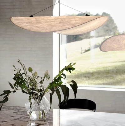 Moderne eetkamer met sculpturale Italiaanse hanglamp van handgeweven stof – elegante verlichting boven marmeren tafel met bloemen en natuurlijke lichtinval.