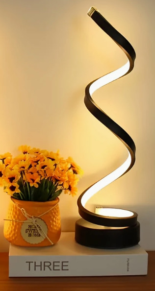 Spiraalvormige zwarte LED tafellamp met warm wit licht en USB-voeding – modern design op een boek naast een gele bloempot, ideaal voor sfeervolle en stijlvolle interieurdecoratie.