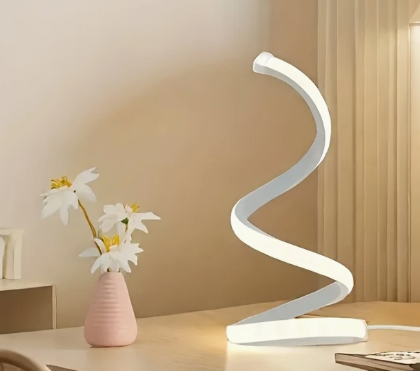 “Witte spiraalvormige LED tafellamp met zacht wit licht – modern design op houten bureau naast roze vaas met bloemen, ideaal voor minimalistische en sfeervolle interieurdecoratie.