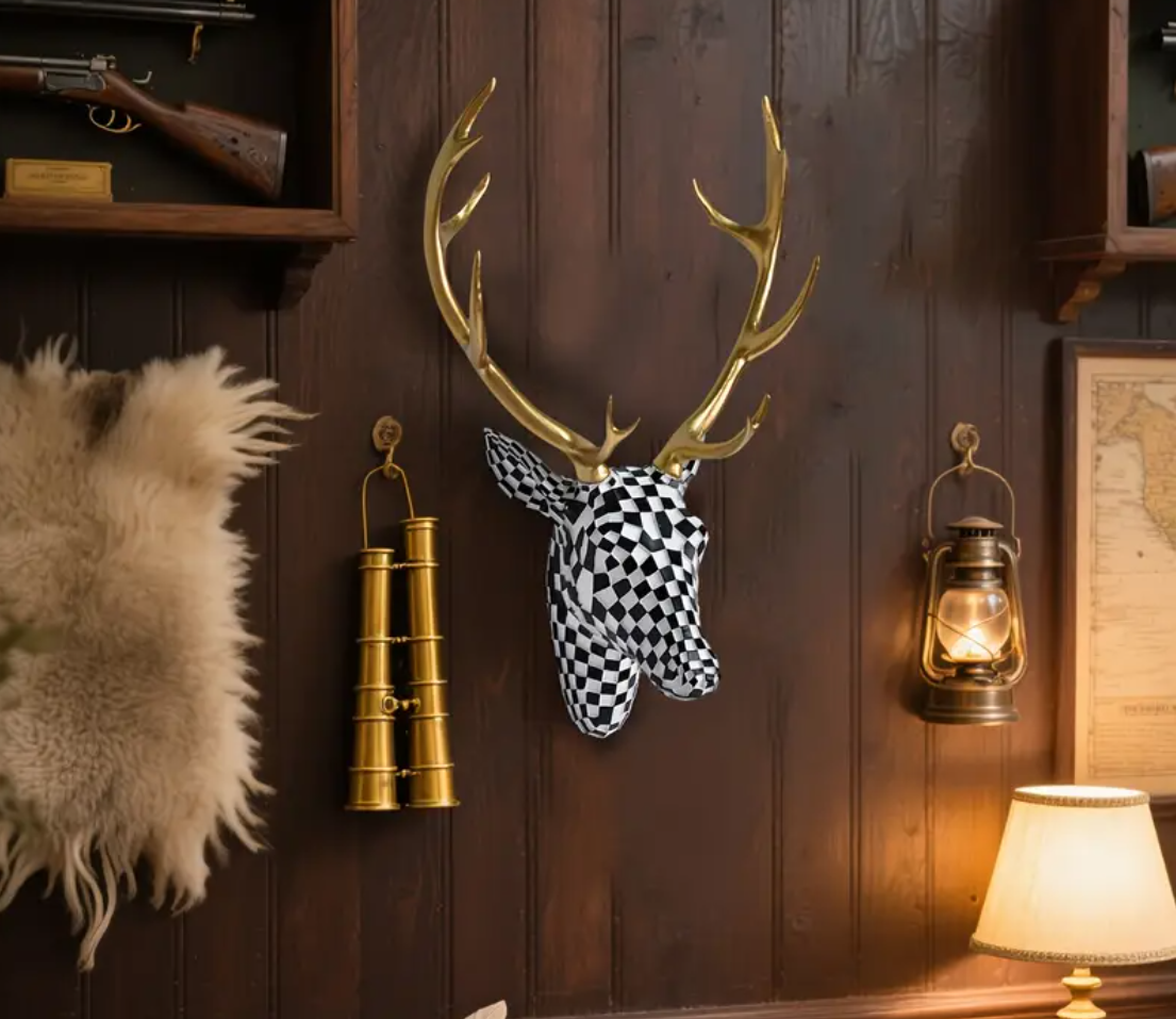 Wanddecoratie van hertenkop in zwart-wit geblokt mozaïekpatroon met glanzende gouden gewei, gemonteerd op donkere houten muur in rustieke setting met vintage details zoals gouden verrekijker, antieke olielamp, geweer op wandplank en beige tafellamp; een opvallend en artistiek accent met modern flair in lodge-achtige sfeer