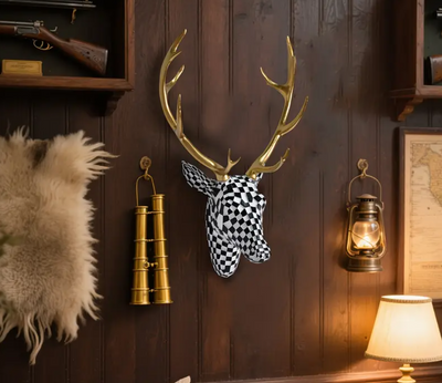 Wanddecoratie van hertenkop in zwart-wit geblokt mozaïekpatroon met glanzende gouden gewei, gemonteerd op donkere houten muur in rustieke setting met vintage details zoals gouden verrekijker, antieke olielamp, geweer op wandplank en beige tafellamp; een opvallend en artistiek accent met modern flair in lodge-achtige sfeer