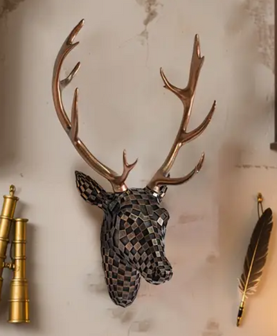 Wanddecoratie van hertenkop in zwart-wit geblokt mozaïekpatroon met glanzend gouden gewei, gemonteerd op lichte muur naast goudkleurige verrekijker en decoratieve veer; een stijlvolle combinatie van moderne kunst en avontuurlijke elementen in eigentijdse setting