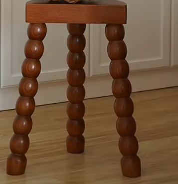 Houten krukje met vier bolvormige, sculpturale poten en een rechthoekige zitting, geplaatst op een houten vloer voor witte paneelkasten. Het unieke ontwerp doet denken aan gestapelde houten kralen — een artistiek en functioneel accent in een moderne keuken- of eetruimte.