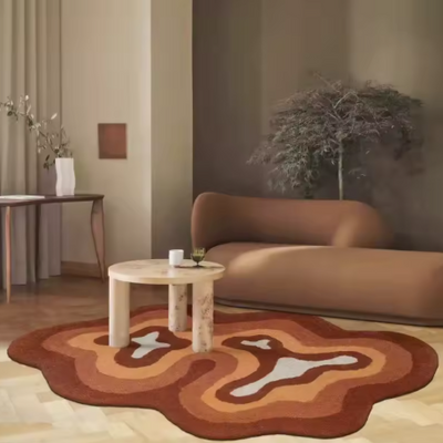 Moderne woonkamer met bruin gebogen sofa en ronde houten salontafel, gedecoreerd met witte beker en potje; salontafel geplaatst op vloerkleed met abstract patroon in bruin, oranje en wit tinten; achtergrond toont houten console met witte vaas, plant met dunne takken en klein rechthoekig wanddecor, naast lichte gordijnen en houten vloer; een warme, stijlvolle setting met natuurlijke materialen en organische vormen