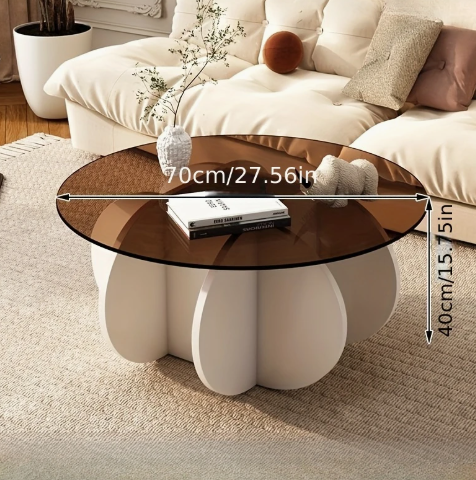 Luxe ronde salontafel met bruin glazen blad en sculpturaal wit onderstel in bloemvorm, diameter 70 cm en hoogte 40 cm; geplaatst op beige vloerkleed in moderne woonkamer met witte sofa en kussens; tafel gedecoreerd met witte pot met groene plant, een elegante en stabiele eyecatcher die lichter oogt in werkelijkheid en perfect past in een exclusief interieur