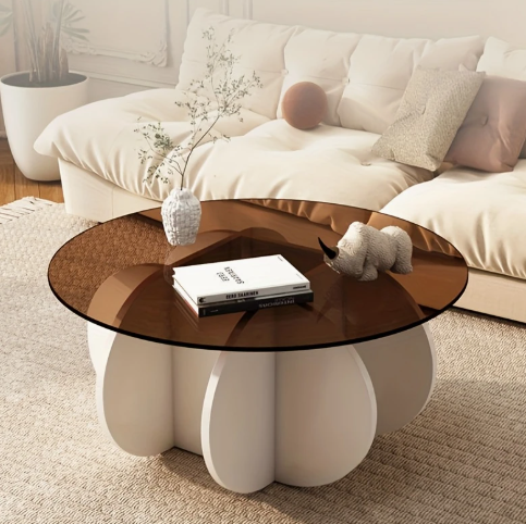Luxe ronde salontafel met bruin glazen blad en sculpturaal wit onderstel in bloembladvorm, afgebeeld in moderne woonkamer met witte sofa en beige vloerkleed; tafel gedecoreerd met designboek, vaas met groene plant en kleine decoratieve neushoorn, een verfijnd en elegant middelpunt voor exclusief interieur, waarbij het glazen blad lichter oogt in werkelijkheid