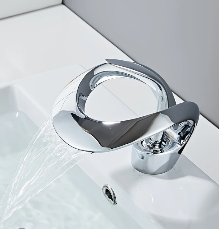 Moderne wastafelkraan met chroomafwerking en open spuitmond, gemonteerd op witte wastafel; water stroomt in een elegante boog in de zichtbare afvoer, een artistiek en functioneel ontwerp dat hedendaagse badkamerinrichting verrijkt met visuele flair en strakke lijnen