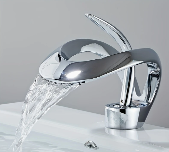 Design wastafelkraan in chroomafwerking met elegant gebogen bladvormige uitloop en bijpassende hendel, gemonteerd op witte wastafel met stromend water; de kraan contrasteert subtiel met de lichtgrijze achterwand, een stijlvolle combinatie van organische vorm en moderne functionaliteit voor hedendaags badkamerdesign