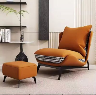 Loungefauteuil met bijpassende ottoman, uitgevoerd in oranje kunstleer met pied-de-pouleprint op de zijpanelen en rugzijde; het zitmeubel is geplaatst in een modern interieur met beige wand, licht vloerkleed, zwarte ronde bijzettafel met plant en glas, en wandplanken met boeken en decoratie; het geheel straalt moderne elegantie en comfort uit, perfect voor woonkamer of relaxhoek