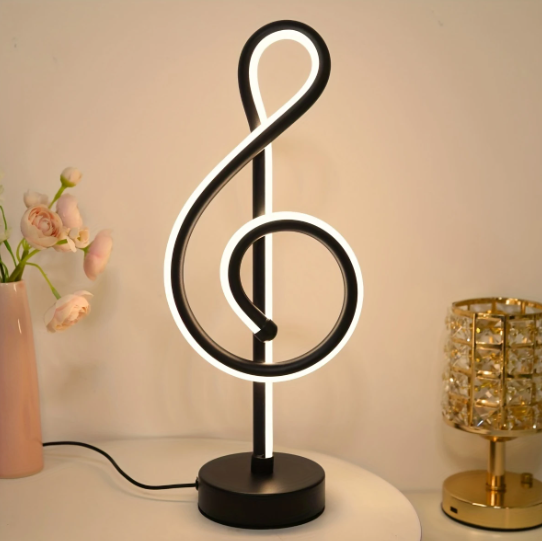 Decoratieve LED-lamp in de vorm van een solsleutel van zwart acryl met geïntegreerde witte LED-lichtlijn op ronde voet; staat op een wit tafelblad naast een roze vaas met lichtroze bloemen en een gouden kristalobject; kabel zichtbaar.