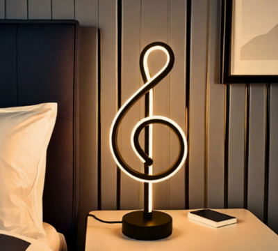 Decoratieve LED-lamp in de vorm van een solsleutel met warme witte lichtlijn op zwarte voet, op een houten nachtkastje naast een smartphone; achtergrond van verticale houten panelen, wit kussen en donkergrijs hoofdeinde.