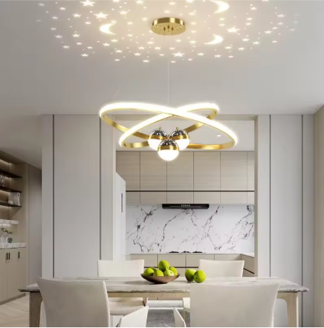 Nordic LED-kroonluchter met gouden interlockende ringen en geïntegreerde LED-bollen, sfeervolle sterren- en maanprojectie, hangend boven een eettafel met schaal groene appels en vier stoelen in een moderne eetkamer met marmeren achterwand