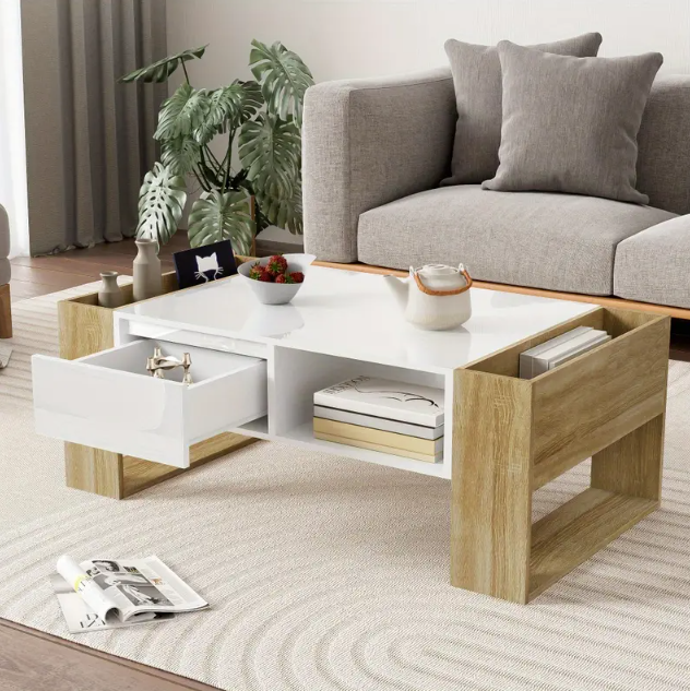 Moderne koffietafel van 105 cm met wit blad, houtkleurige zijkanten en deels open onderzijde met lade en vakken; lade half geopend, bovenzijde gedecoreerd met witte theepot, glazen schaal met rode bessen en kleine plant in pot; geplaatst op licht vloerkleed met cirkelmotief naast grijze sofa met kussens, een functioneel en decoratief middelpunt voor eigentijdse woonkamer