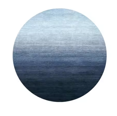 Circulair vloerkleed met subtiel, gelijkmatig kleurverloop van lichtblauw (boven) naar donker marineblauw (onder); het ronde Nordic Blue Haze-kleed is vervaardigd uit zachte synthetische vezels en heeft een antislip-onderzijde; het minimalistische ontwerp en de serene tinten brengen rust en een artistiek accent in moderne woon- of slaapruimtes
