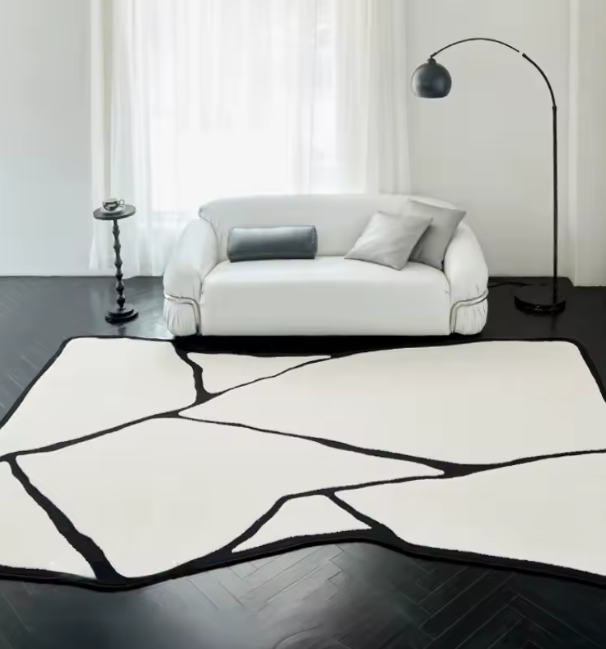 Moderne woonkamer met witte sofa en twee kussens, vloerlamp met zwart gebogen frame en halfronde kap, en opvallend vloerkleed met abstract patroon; het tapijt toont witte vormen omlijnd in zwart, als gebroken scherven of eilandstructuren, geplaatst op donker houten vloer bij groot raam met witte transparante gordijnen; een stijlvol en grafisch interieur met sterke contrasten en natuurlijke lichtinval